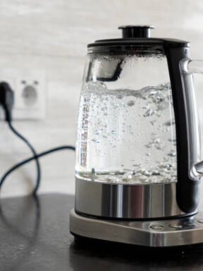 Transparent electric kettle with boiling water on table in the kitchen